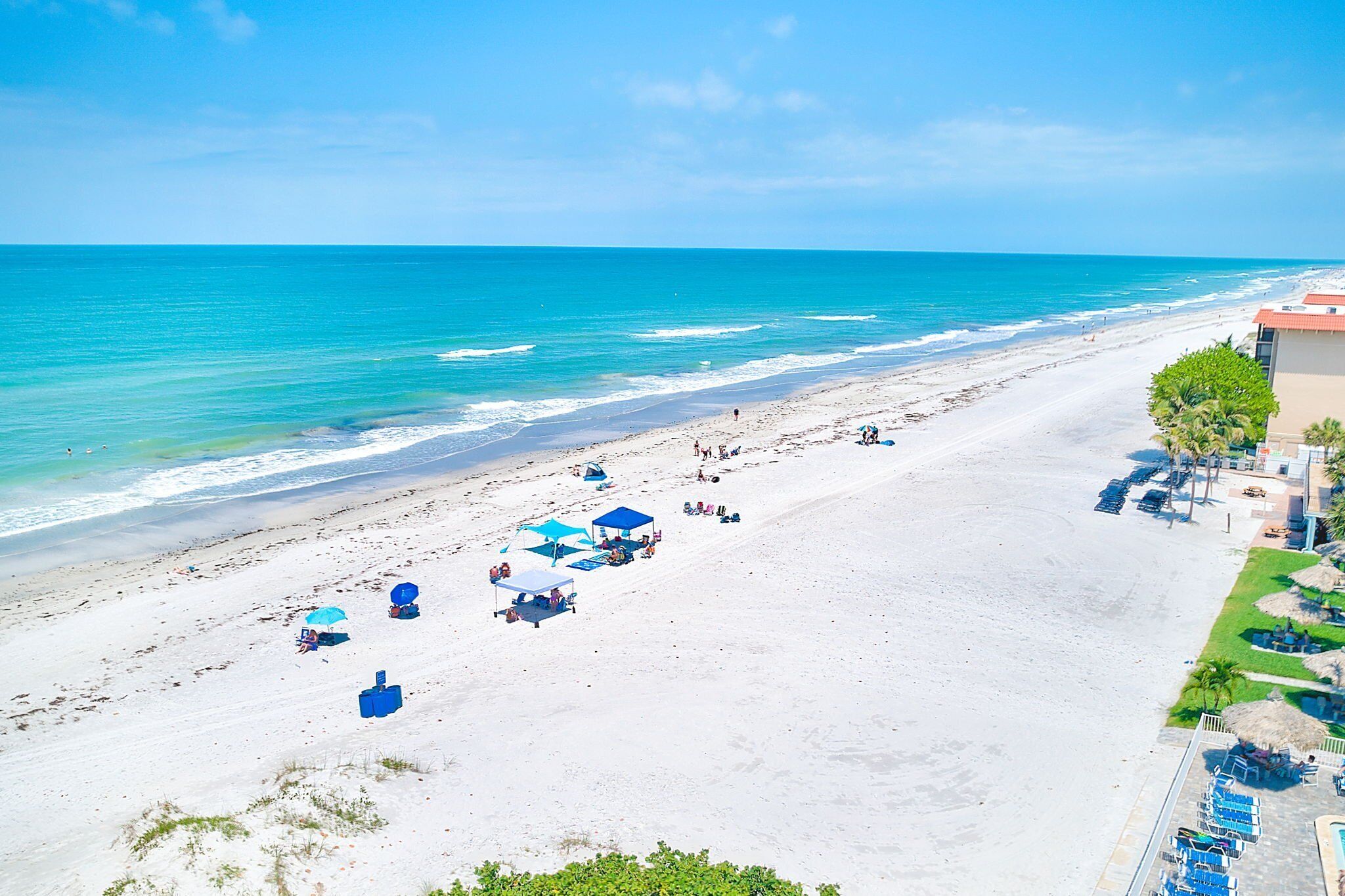 A beach with clear blue water, a sandy shore, and a few umbrellas and lounge chairs.
