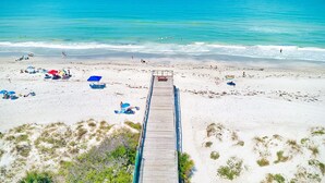 A beach with a wooden walkway leading to the water, surrounded by sand and sparse vegetation. - Beachside & Amazing Views! 3BR/3BA, Heated Pool/Spa  606 (Redington Shores)