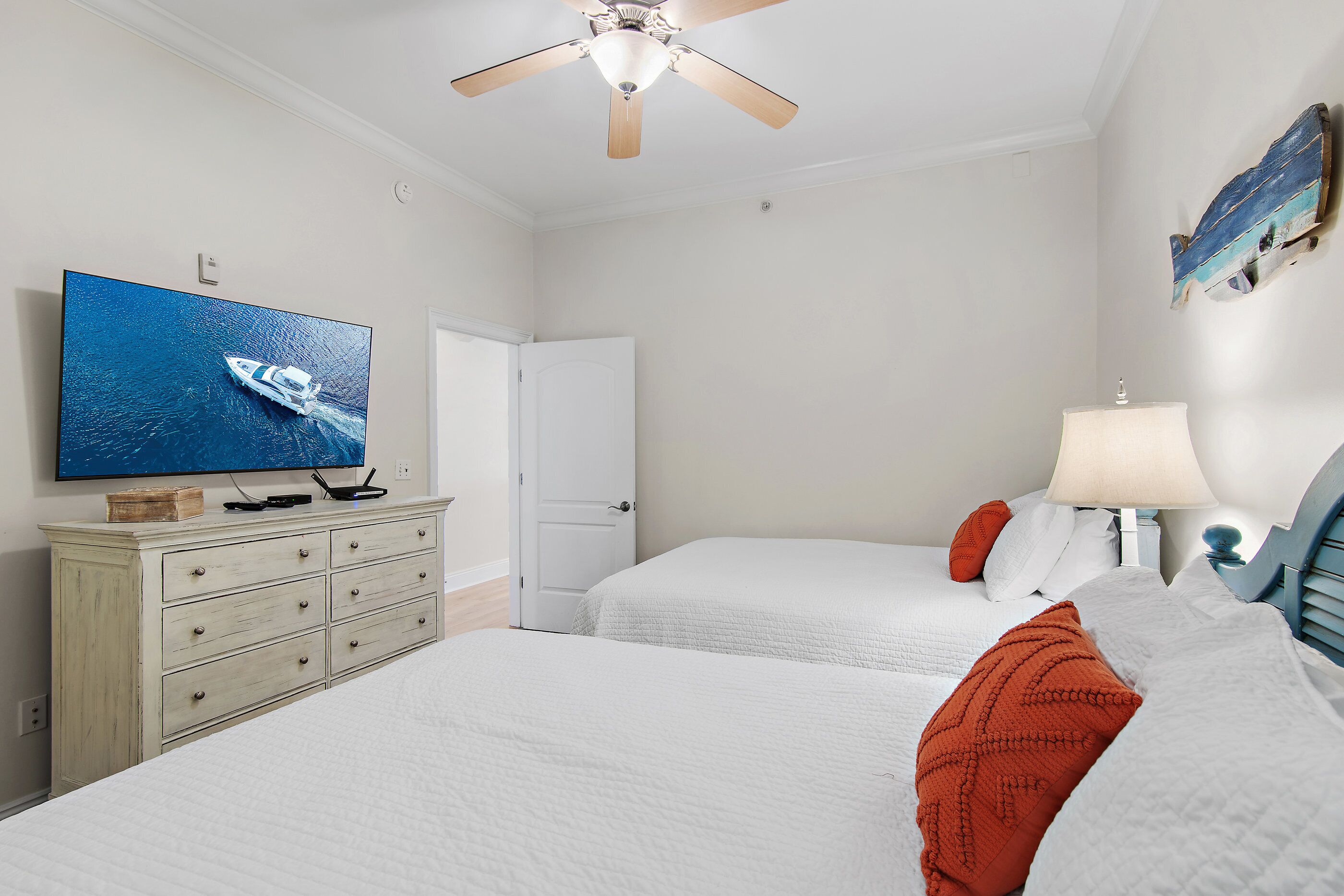 Quarto de hotel com duas camas, uma televisão em uma cômoda, um ventilador de teto e uma porta.