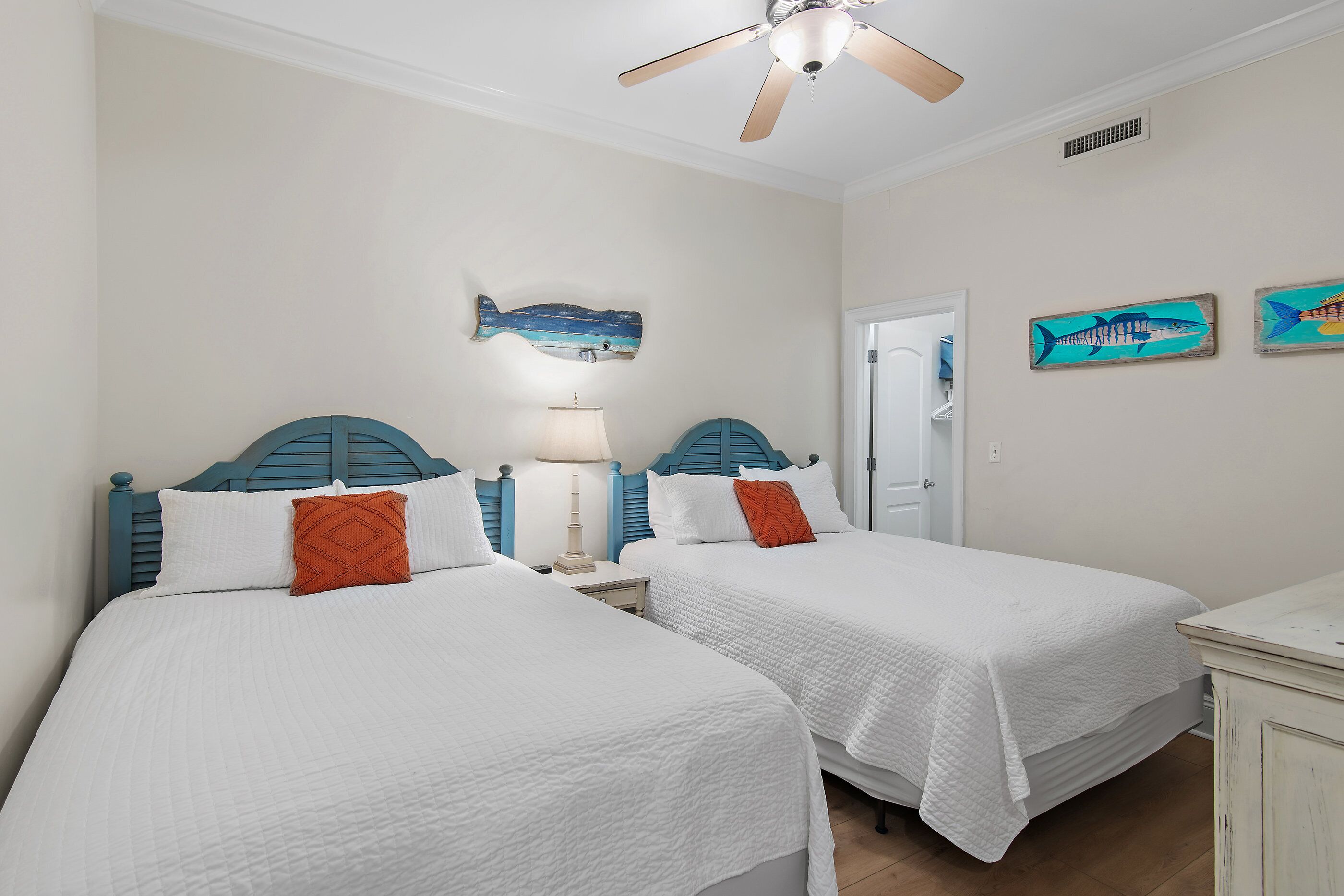 A room with two beds, a ceiling fan, and wall art of fish.