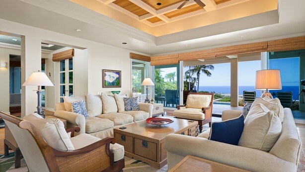 Amplio salón con una gran ventana con vistas al océano, amoblado con sofás, sillones y una mesa de centro color beige.