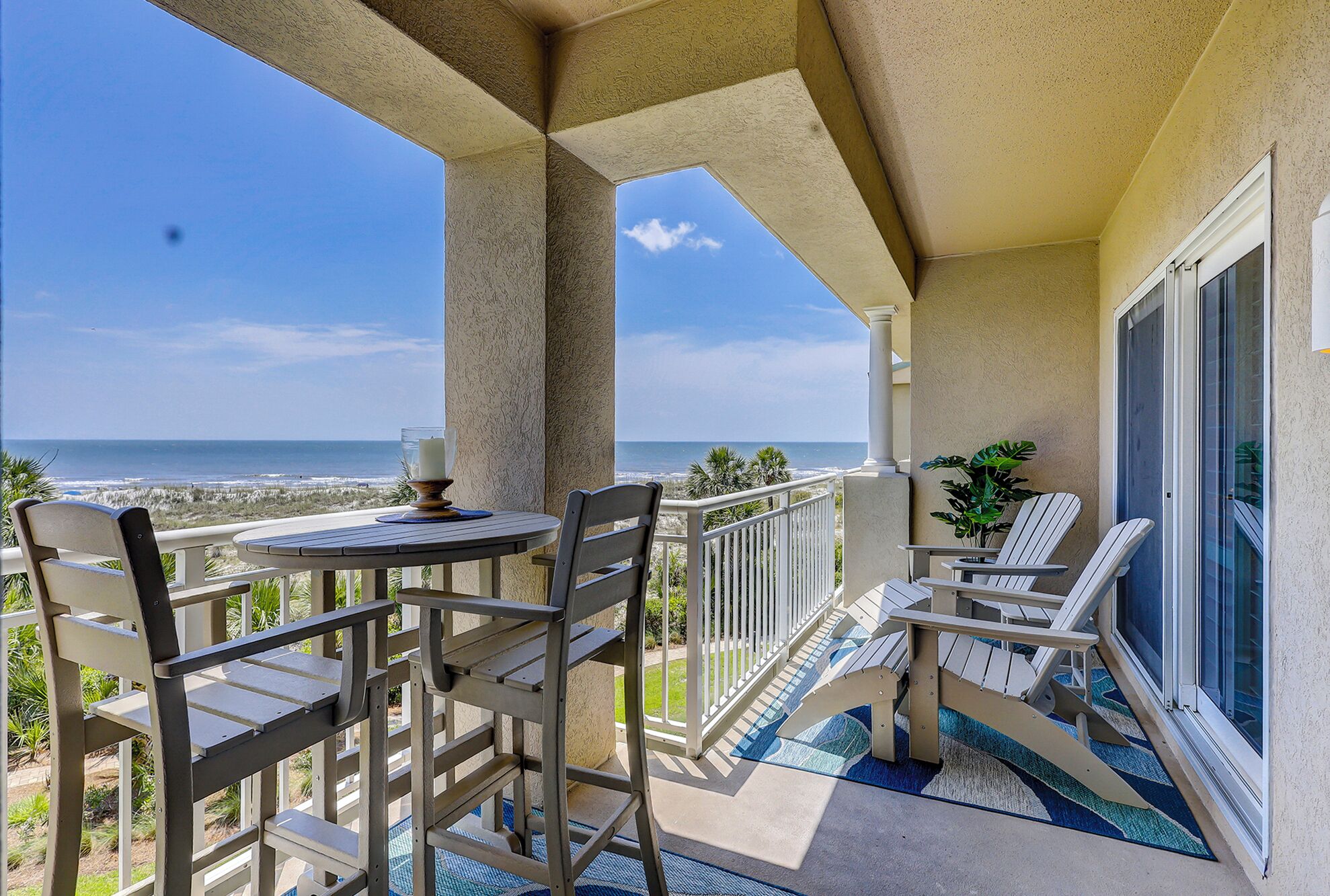 A balcony with a table and chairs, a view of the ocean, and a potted plant.