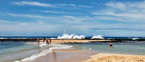 A beach with clear skies, waves crashing onto the shore, and people enjoying the water.
