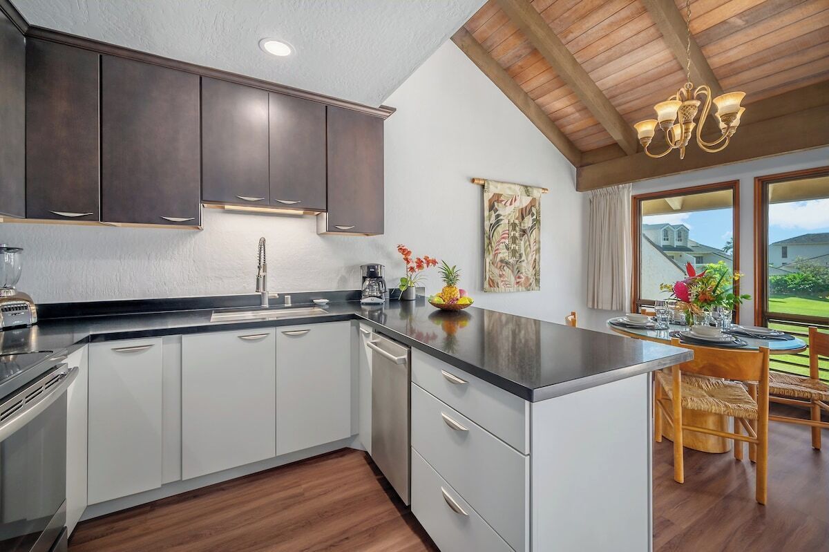 A modern kitchen with dark cabinets, a central island, and a dining area with a view.