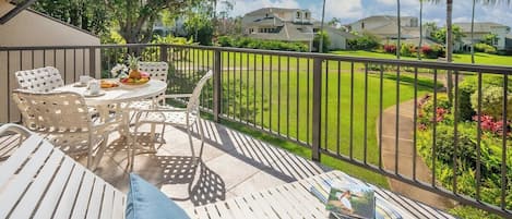 A balcony with white furniture, a table with a fruit bowl, and a magazine.