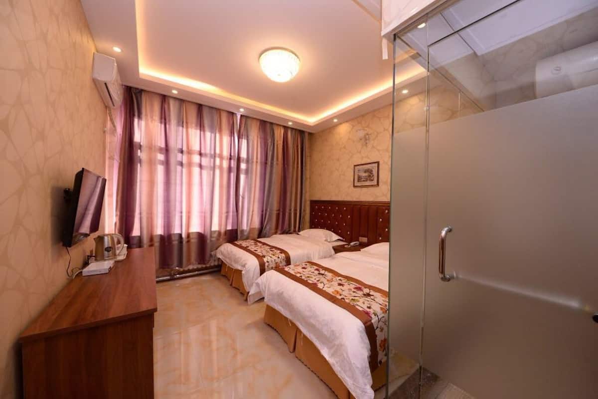 Ein Hotelzimmer mit zwei Betten, einem Schreibtisch, einem Fernseher und einer Dusche.