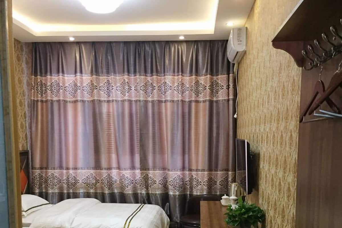 Ein Hotelzimmer mit zwei Betten, einem Schreibtisch, einem Stuhl, einer Zimmerpflanze und einer Holzvertäfelung.