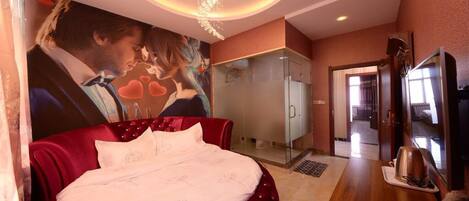 A bedroom with a large bed, a glass-enclosed shower, a television, and a wall-mounted artwork.