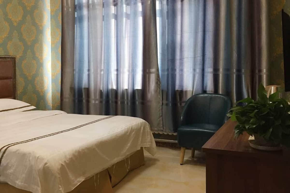 Ein Hotelzimmer mit einem Bett, einem Schreibtisch, einem Stuhl und einem großen Fenster mit Vorhängen.