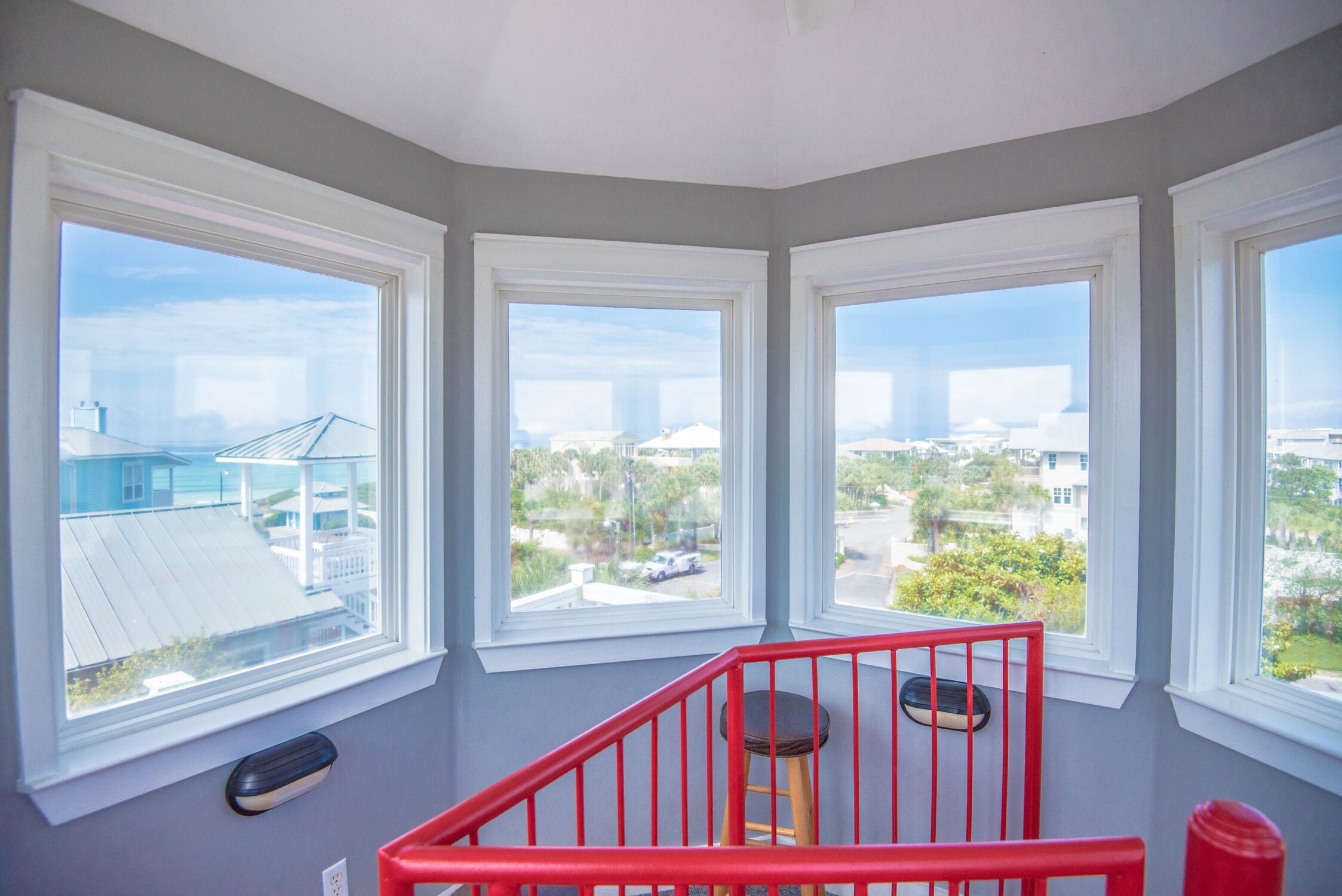 A corner room with three large windows, a red railing, and a view of the cityscape.