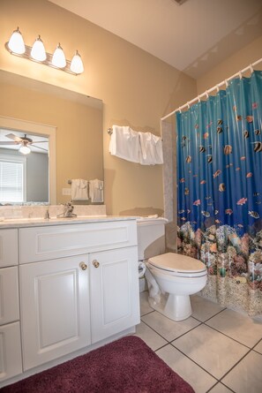 A bathroom with a white vanity, a mirror, a ceiling fan, a toilet, and a shower curtain with a fish pattern. - On Beach Side, Gated neighborhood, All King Beds, Pool, Santa Rosa beach (Santa Rosa Beach)
