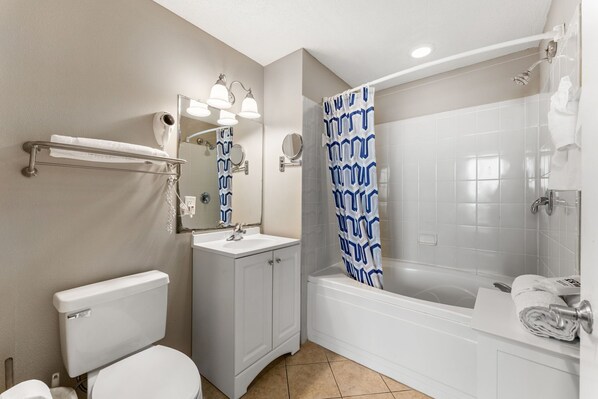 A bathroom with a toilet, sink, mirror, and shower.