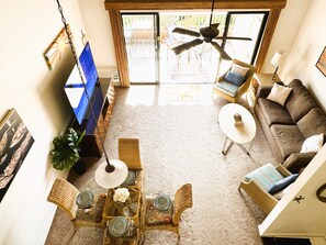 Een woonkamer met een bank, stoelen, een eettafel, een televisie en een plafondventilator.