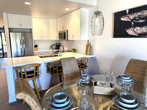 A modern kitchen with white cabinets, stainless steel appliances, and a dining area with wicker chairs and glass tables.