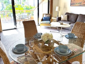 A dining area with a glass table set for four, surrounded by wicker chairs.