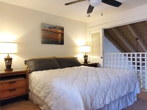 Een slaapkamer met een groot bed, twee bedlampen, een schilderij aan de muur en een houten plafondventilator.