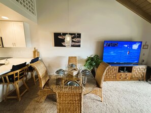 A dining area with wicker furniture, a glass-top table, and a television displaying a sports event.