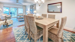 A dining area with a wooden table and wicker chairs, a chandelier, and a large mirror on the wall.