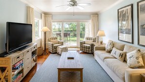 A living room with a television, sofa, armchairs, a coffee table, and a ceiling fan.