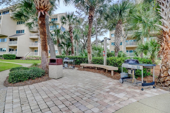 A paved outdoor area with palm trees, a barbecue grill, and a bench. - 457 Captains Walk- Just walk out your living area to the beach. (Hilton Head Island)