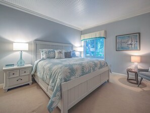 Een slaapkamer met een bed, nachtkastjes, een raam met zonwering, een schilderij en een stoel.
