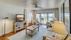 Ein geräumiges Wohnzimmer mit Fernseher, Sofa und Deckenventilator.