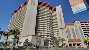 Un hotel moderno de altura con varios balcones, palmeras y un letrero que anuncia Playa Panama City.