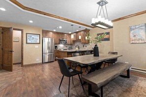 Une cuisine moderne avec des meubles en bois, un réfrigérateur en acier inoxydable et un coin repas comprenant une table et des bancs en bois.