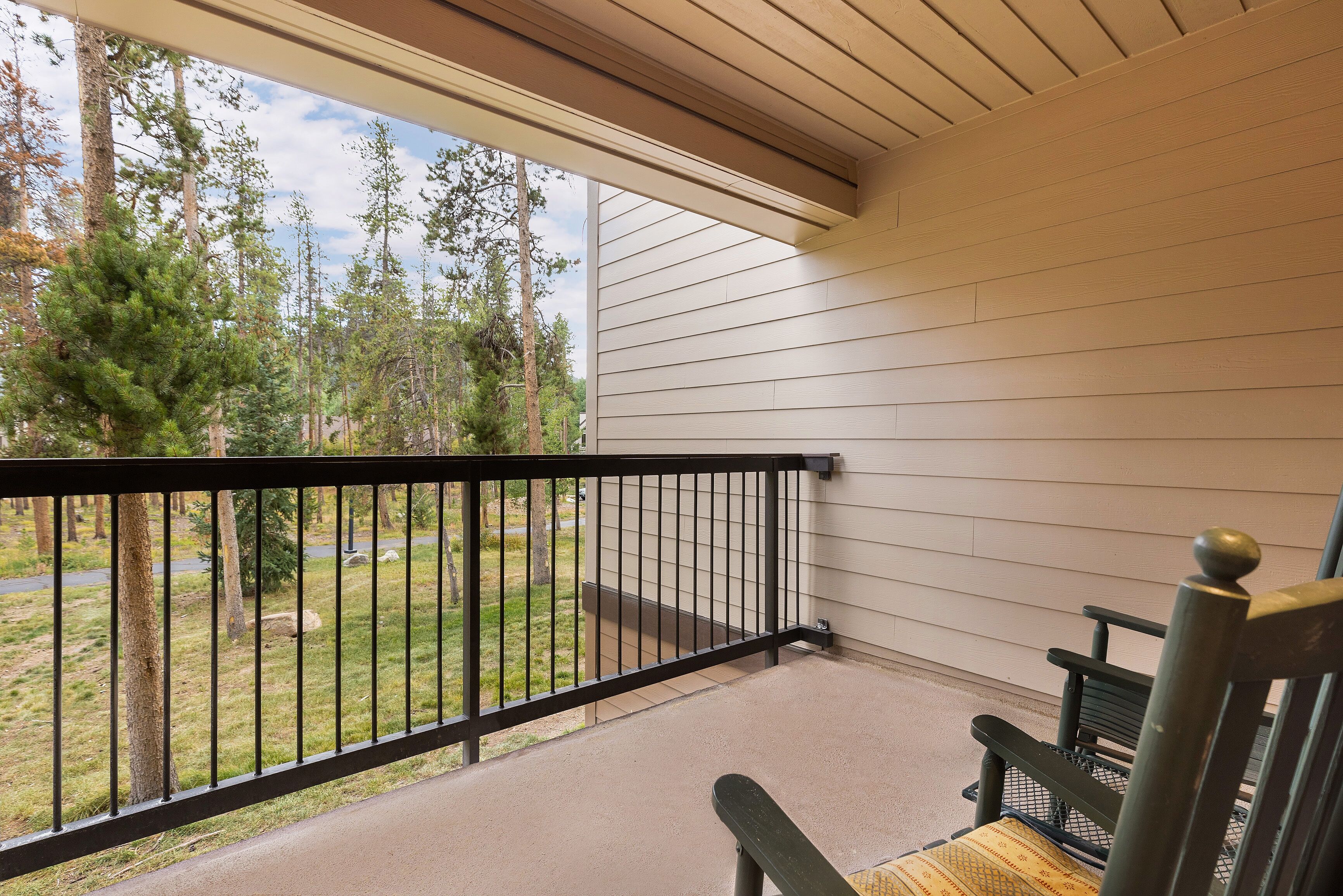A covered porch with a black railing, a bench, and a view of a wooded area.