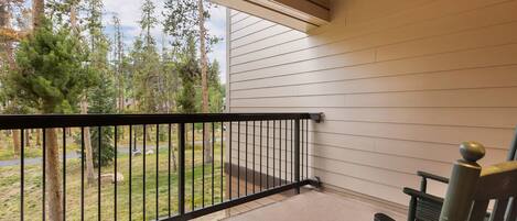 A covered porch with a black railing, a bench, and a view of a wooded area.