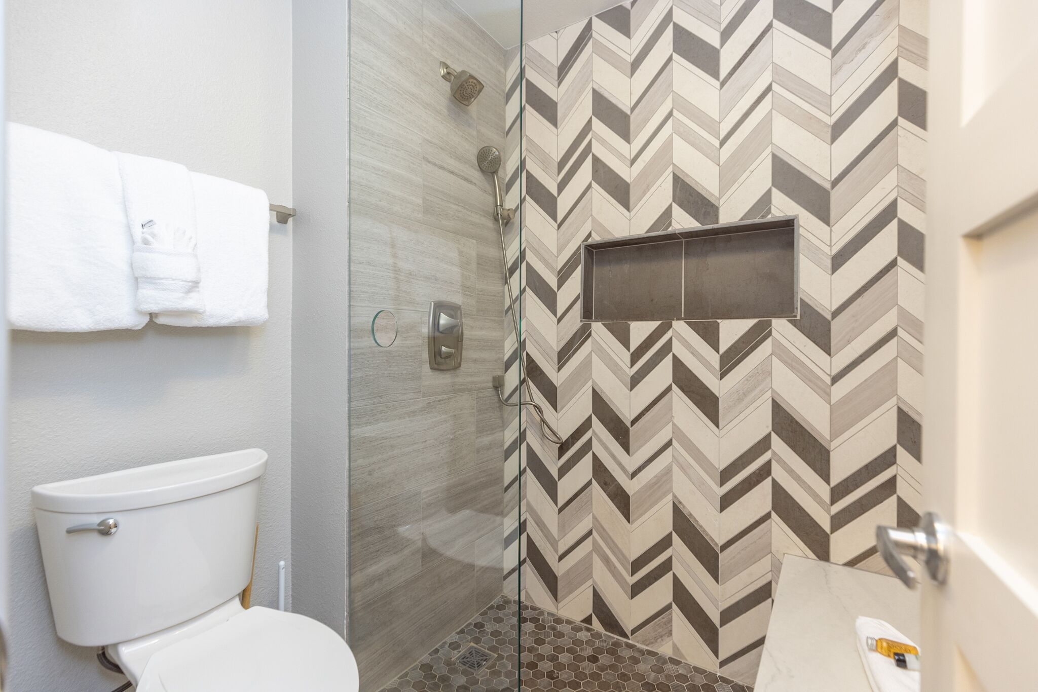 A bathroom with a toilet, a shower with a glass door, and a tiled wall with a chevron pattern.