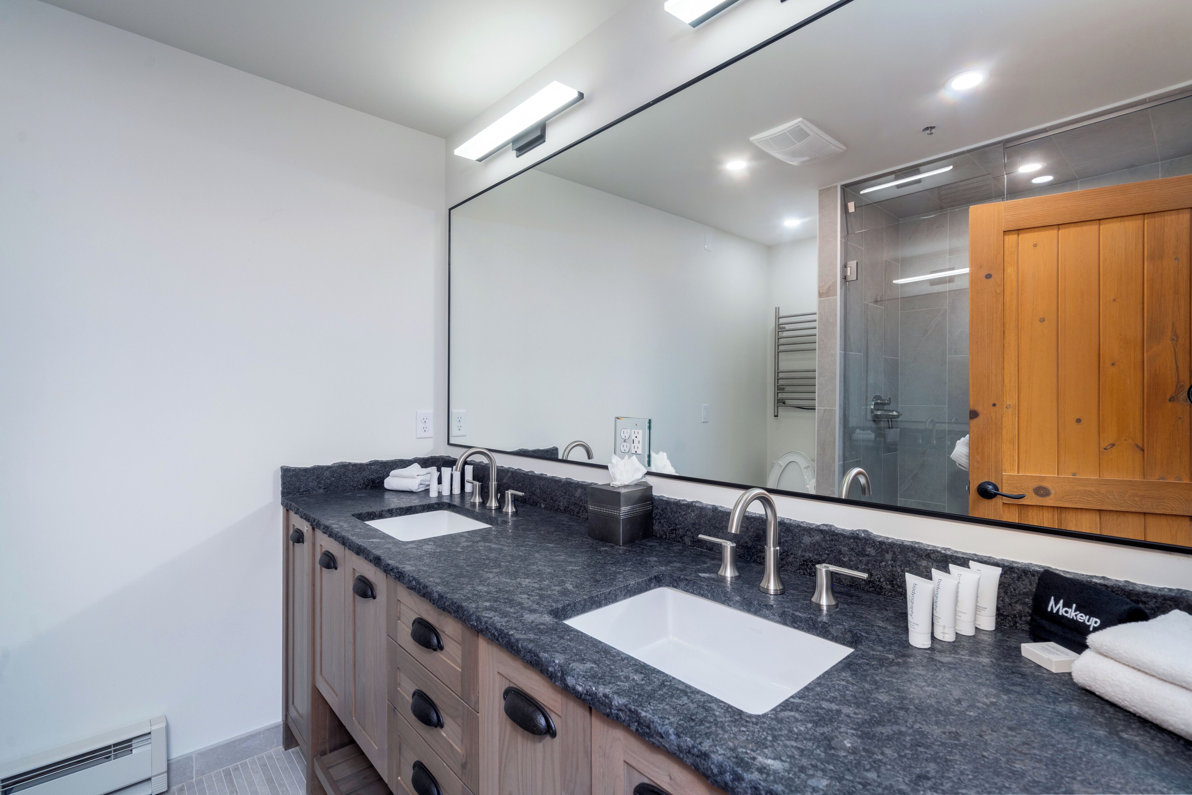 Un bagno moderno con due lavabi, uno specchio grande e una porta in legno.