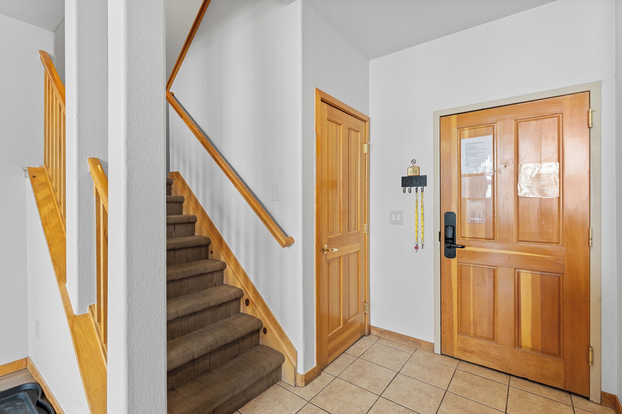 A staircase with wooden handrails, a wooden door with a peephole, and a wall-mounted light switch.