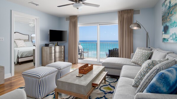 A spacious living room with a balcony overlooking the ocean, a television, and a comfortable seating area.
