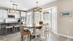A spacious kitchen with white cabinets, a wooden dining table, and wicker chairs. - ☀Private Pool~Across from Gulf~Carriage House~5BR Ocean Breezes🌅 (Destin)