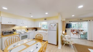 A modern kitchen with white cabinets, a dining table with chairs, and a view of the outdoor patio area.