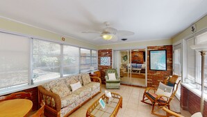 A sunlit room with a sofa, chairs, a table, and a ceiling fan.