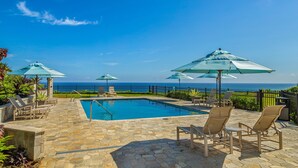 A pool area with lounge chairs and umbrellas, a stone patio, and a view of the ocean. - PUU POA #110 GORGEOUS OCEAN VIEWS AIR CONDITIONED Condo! (Princeville)