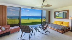 A room with a bed, a sofa, and a table. There is a view of the ocean through large windows. - PUU POA #110 GORGEOUS OCEAN VIEWS AIR CONDITIONED Condo! (Princeville)
