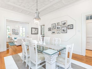 A dining area with a glass-top table, white chairs, and a chandelier.