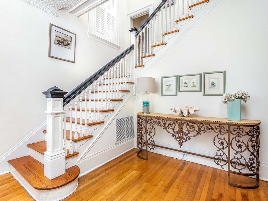 A staircase with white balusters and wooden steps, a console table with decorative metalwork, and framed pictures on the wall.