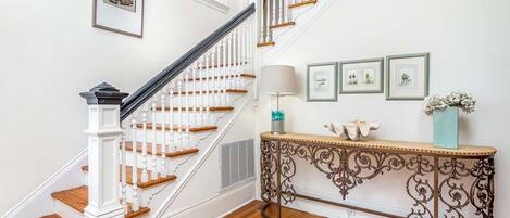 A staircase with white balusters and wooden steps, a console table with decorative metalwork, and framed pictures on the wall.