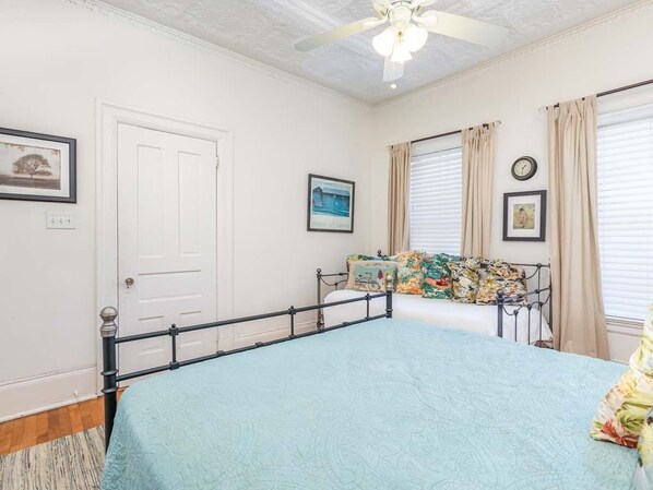 Une chambre à coucher avec un lit, un ventilateur de plafond, une fenêtre avec des rideaux et une porte.