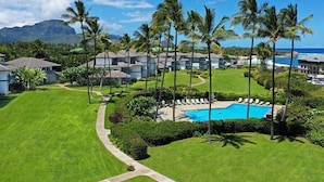 A resort with a swimming pool, palm trees, and a view of the ocean. - Poipu Sands 226  By Suite Paradise (Koloa)