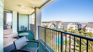 En balkon med udendørs møbler, udsigt over et boligområde og en swimmingpool.