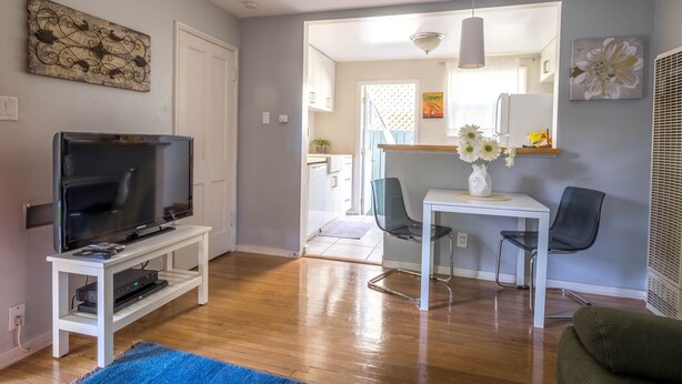 A living room with a TV on a stand, a dining table with chairs, and a blue rug. - Bright one-bedroom bungalow, located near all Pasadena’s best attractions. (Pasadena)