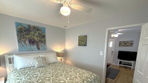 A bedroom with a bed, a ceiling fan, a painting, a TV, and a door leading to another room. - Bright one-bedroom bungalow, located near all Pasadena’s best attractions. (Pasadena)