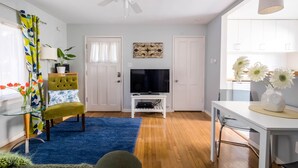A modern living room with a flat-screen TV, a ceiling fan, a dining table, and a blue rug. - Bright one-bedroom bungalow, located near all Pasadena’s best attractions. (Pasadena)