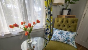 A room with a glass table holding a vase of tulips, a green upholstered chair, and a floral pillow. - Bright one-bedroom bungalow, located near all Pasadena’s best attractions. (Pasadena)
