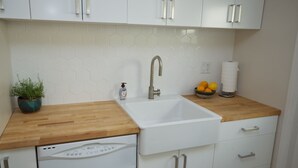 A modern kitchen with white cabinets, a wooden countertop, a built-in dishwasher, a stainless steel sink, and a potted plant. - Bright one-bedroom bungalow, located near all Pasadena’s best attractions. (Pasadena)